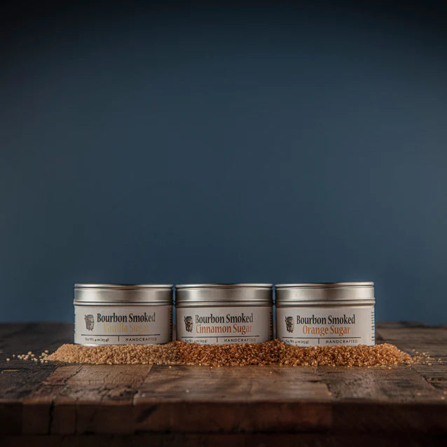 Three tins of bourbon smoked sugar on a wooden surface with a dark blue background
