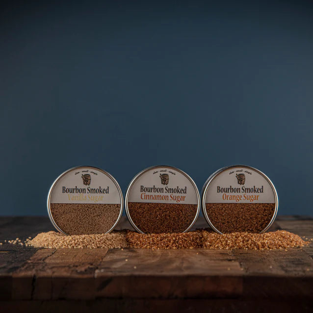 Three containers of bourbon smoked sugar on a wooden surface with a dark blue background
