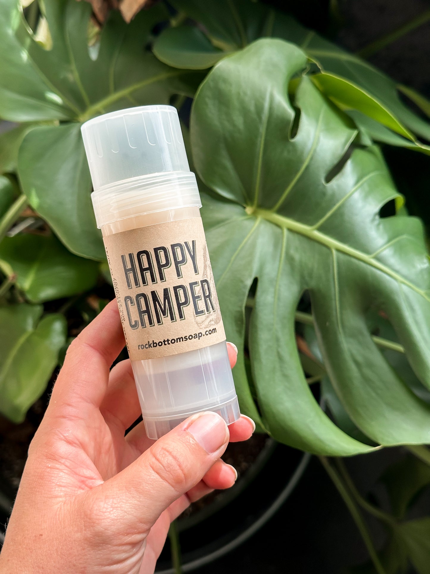 Happy Camper Natural Bug Repellent Lotion Bar displayed over a houseplant – eco-friendly, skin-safe bug protection in solid balm form