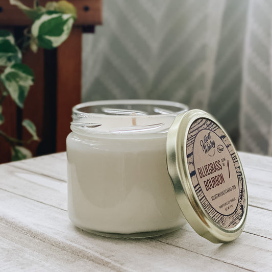 An 11 oz handmade soy wax candle in a clear jar with a gold lid, featuring a single cotton wick and labeled with the scent 'Bluegrass Bourbon'.