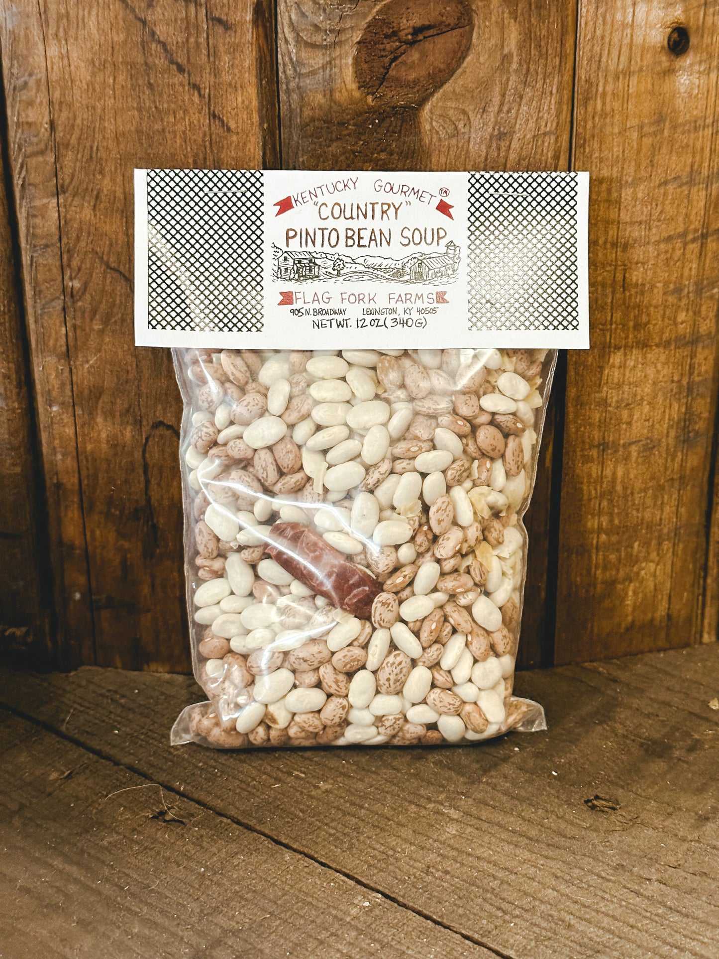 Packaged country pinto bean soup mix in a clear plastic bag with a label on top showing the product name and brand, set against a wooden background.