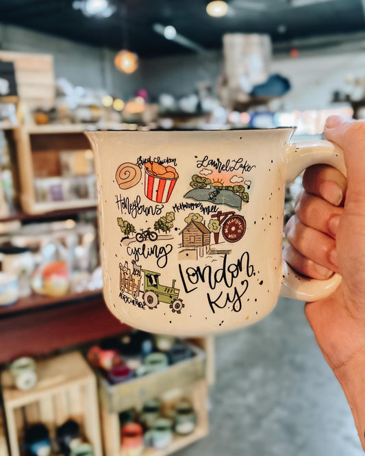 A beige camp mug with London, KY Camp inscribed and various illustrations related to London, such as fried chicken and bicycles.